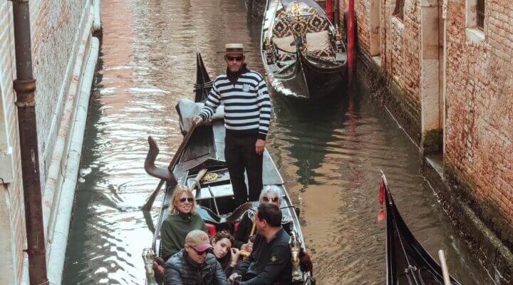 Uomo che guida una barca a Venezia, simbolo della connessione tra brand italiani e produttori di abbigliamento in India, inclusi produttori t-shirt India, produttori felpe con cappuccio India, produttori abbigliamento uomo India e produttori abbigliamento bambini India.